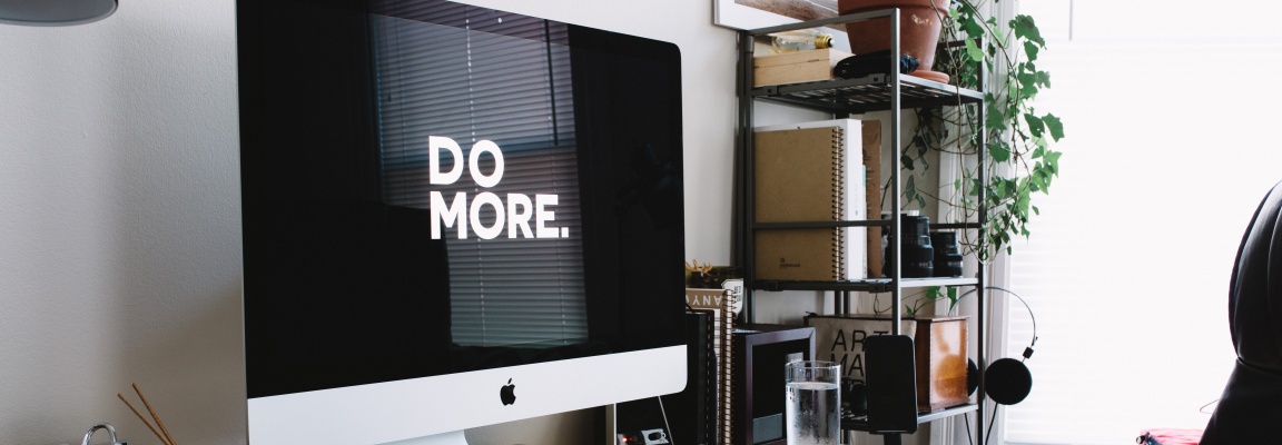 Computer screen on a desk with the words 'DO MORE' in large white letters on a black background
